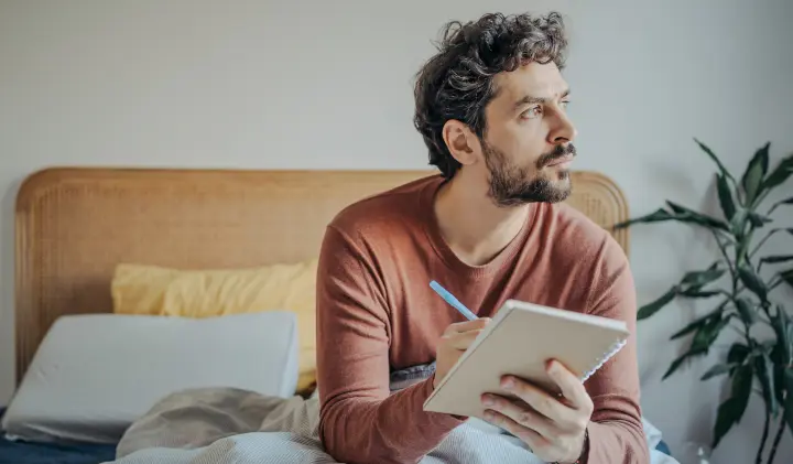 Mann sitzt im Bett und führt Schlaftagebuch