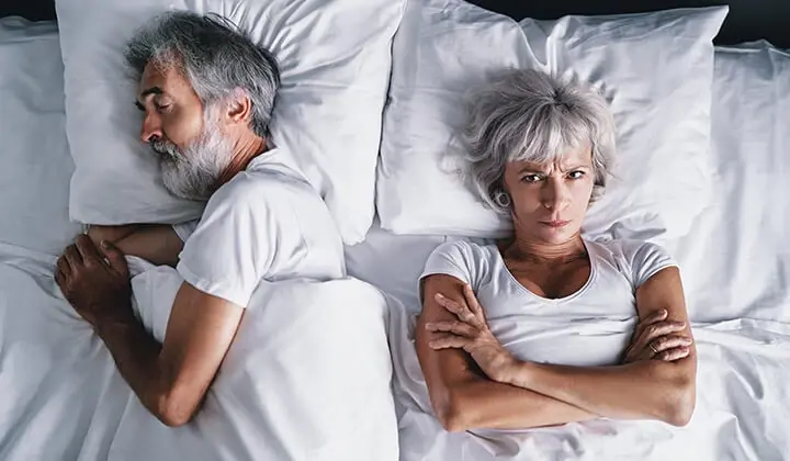 Frau liegt schlaflos im Bett neben schnarchendem Mann